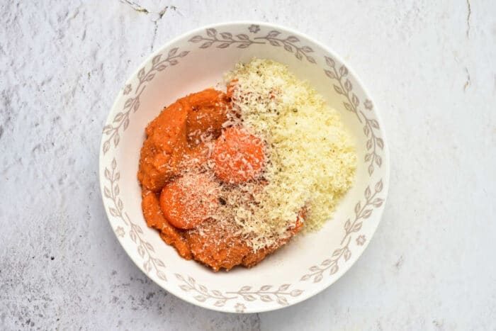 White bowl with tomato sauce and grated cheese, placed on a light marble surface—a good serving suggestion for Pumpkin Spaghetti or Pumpkin Noodles.