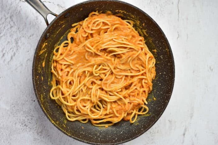 Pumpkin Spaghetti coated in creamy orange sauce sits in a black nonstick pan on a white surface.
