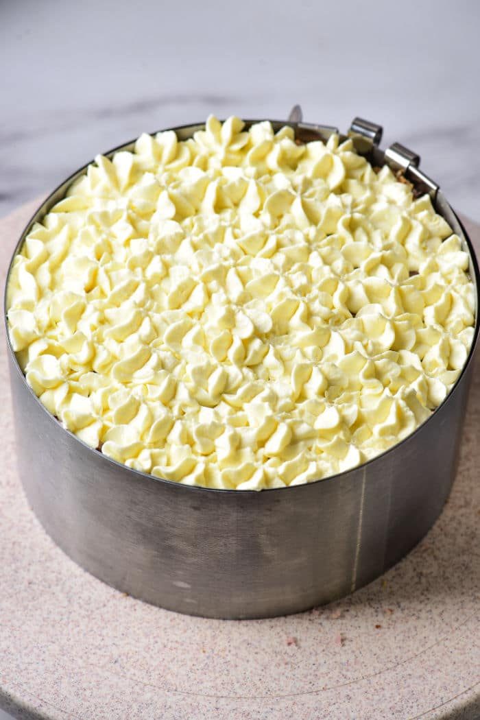 An 8-inch purple cake in a metal mold topped with elegant white frosting swirls.
