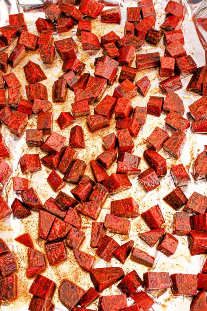 Cubed roasted purple sweet potatoes on a foil-lined baking sheet, seasoned and evenly spread.