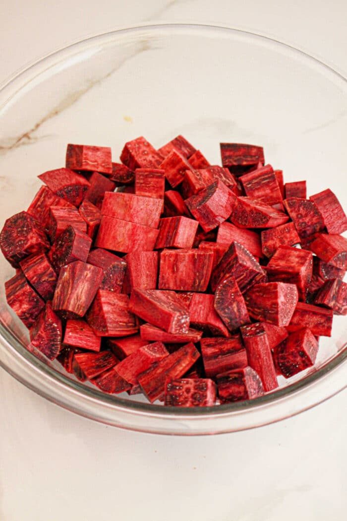 A glass bowl filled with cubed pieces of fresh purple yam, solid for your next purple sweet potato recipe, rests on a white surface.
