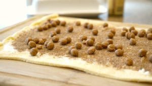 Rolled-out crescent roll dough topped with cinnamon, sugar, and pecans on a wooden board.