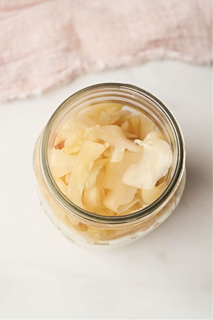 A glass jar filled with marinated cabbage rests on a light fabric background, reminiscent of the subtle simplicity of a quick sauerkraut recipe.