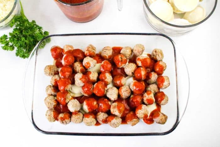 Glass baking dish with meatballs covered in tomato sauce, sliced mozzarella, and parsley on a white surface—solid for serving alongside a homemade Ravioli Casserole.