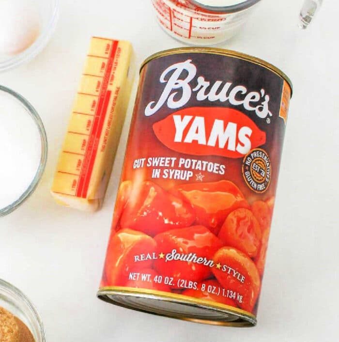 A can of Bruce's Yams, labeled "Cut Sweet Potatoes in Syrup" and "Real Southern Style," solid for a Recipe for Sweet Potato Pie with Sweetened Condensed Milk. The can is 40 ounces (2 lbs 8 oz / 1.134 kg). Nearby are a stick of butter, a measuring cup, and other cooking ingredients.