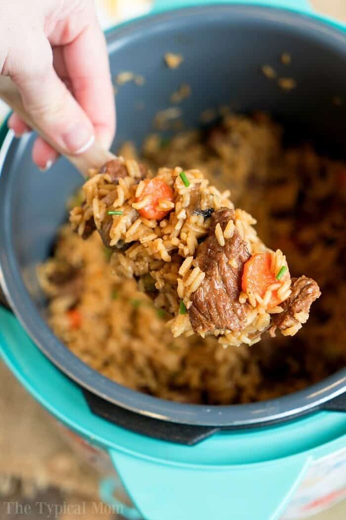 A hand holding a spoonful of beef stew meat and rice from a rice cooker, showcasing a good creation inspired by recipes using beef stew meat.
