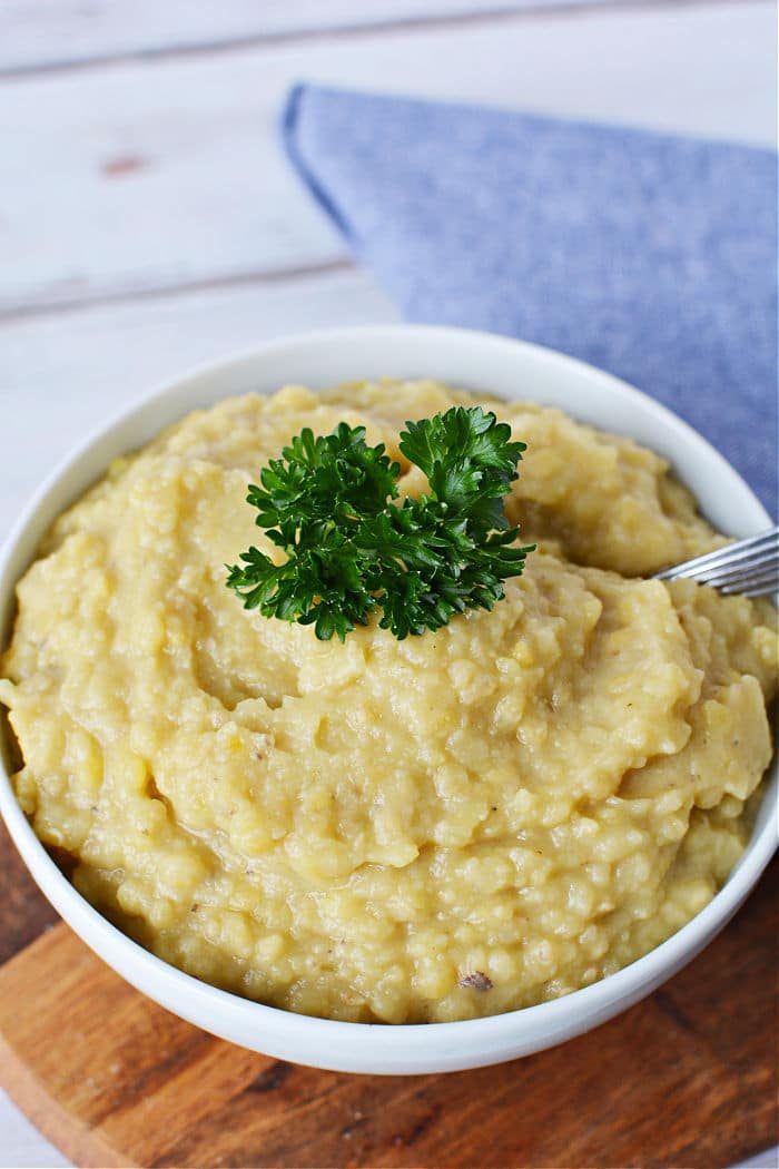 Bowl of creamy red lentils, garnished with fresh parsley, set on a wooden board alongside a blue napkin.