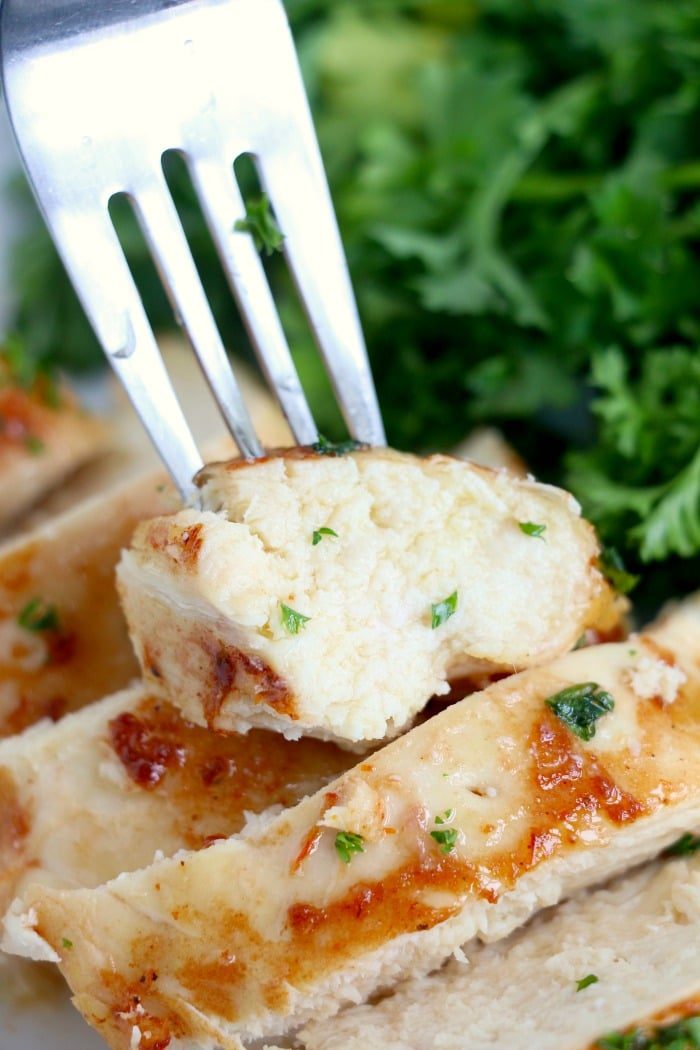 A fork holds a piece of juicy chicken breast, perfectly cooked in the Ninja Foodi, garnished with chopped herbs. The chicken is sliced with visible grill marks. Fresh green parsley or cilantro adorns the background, enhancing its visual appeal.