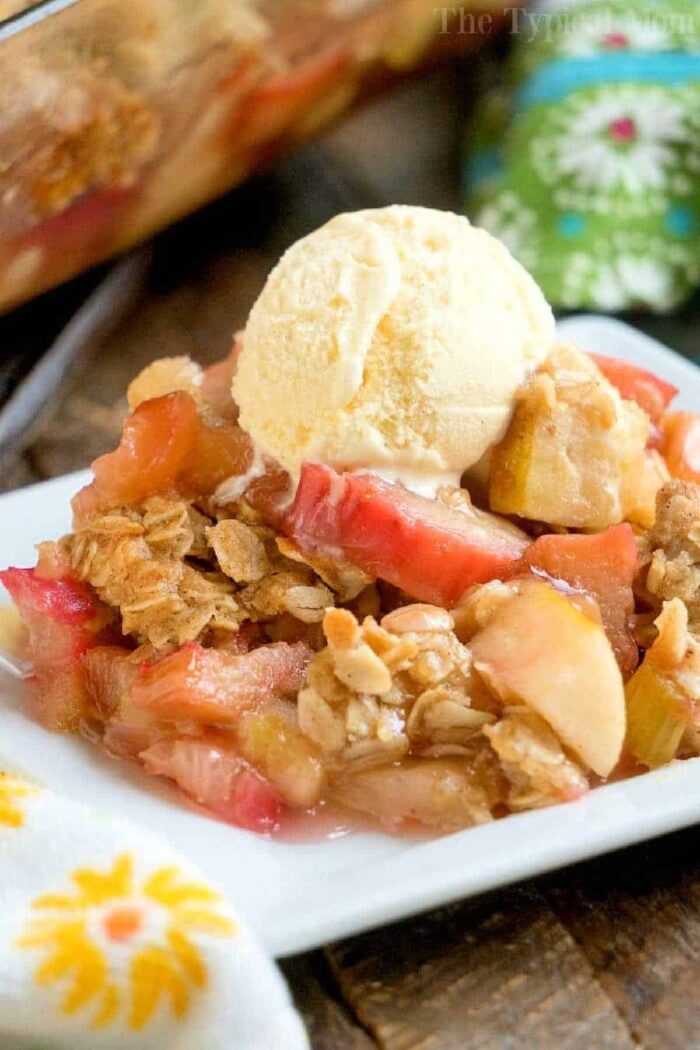 A slice of rhubarb crunch topped with a scoop of vanilla ice cream on a white plate.