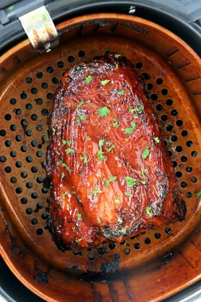 Glazed piece of cooked meat, like juicy ribs in Air Fryer Ninja, garnished with herbs in an air fryer basket.