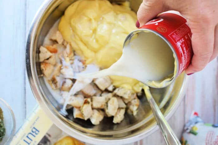 A hand pours canned milk into a bowl with diced chicken and creamy yellow sauce, preparing a good mixture for Ritz Chicken Casserole.