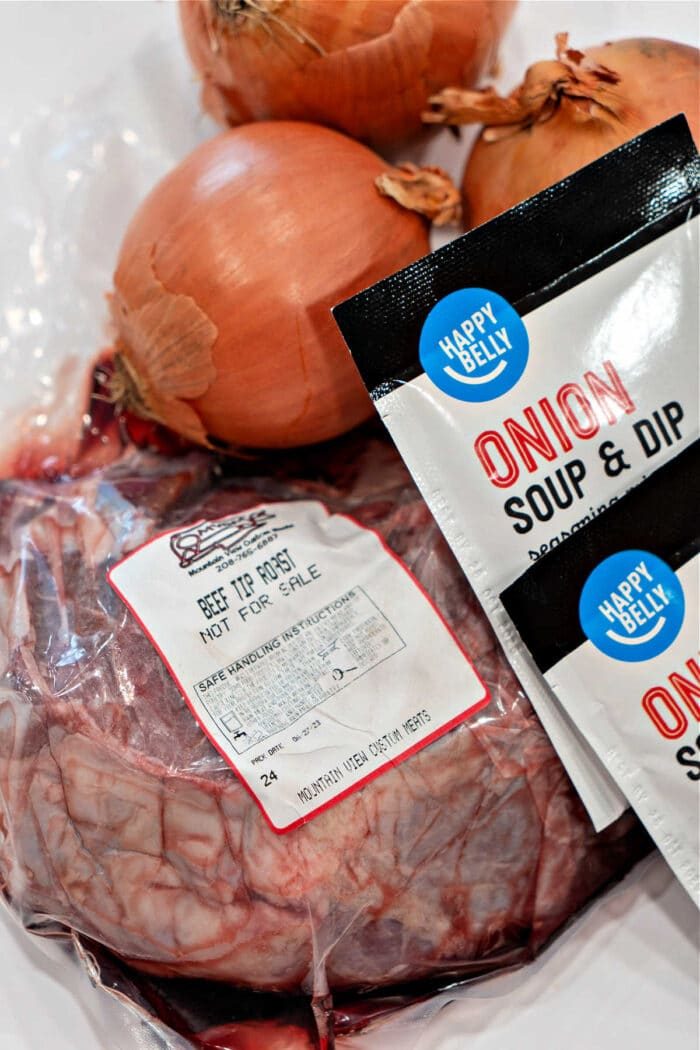 A good blend of packaged beef tip roast and savory onion soup mix packets, complemented by fresh onions, awaits on the kitchen counter.
