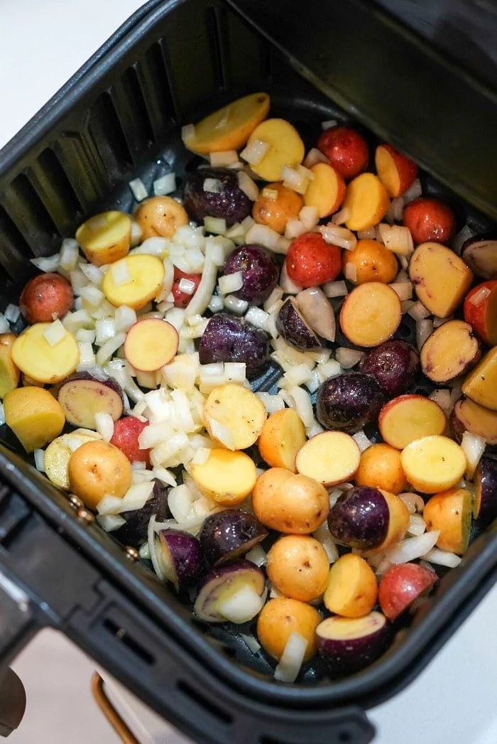 Roasted potatoes in an air fryer, mixed with vibrant chopped onions, are perfectly arranged in the basket and ready for cooking.