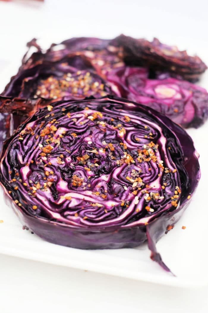 Sliced, roasted red cabbage rounds with seasoning on a white plate.