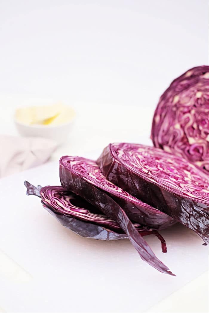 Sliced red cabbage on a white cutting board, solid for preparing Roasted Red Cabbage, with a blurred bowl in the background.