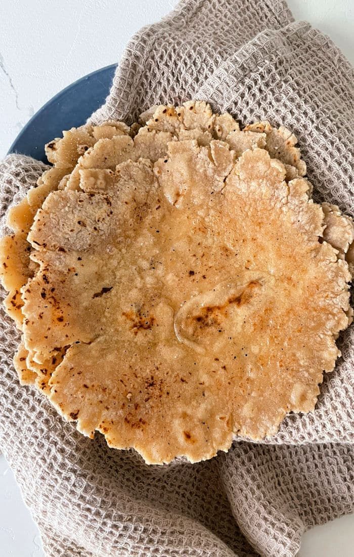 Close-up of homemade roti flatbreads stacked on a textured cloth, showcasing the art of how to make roti.