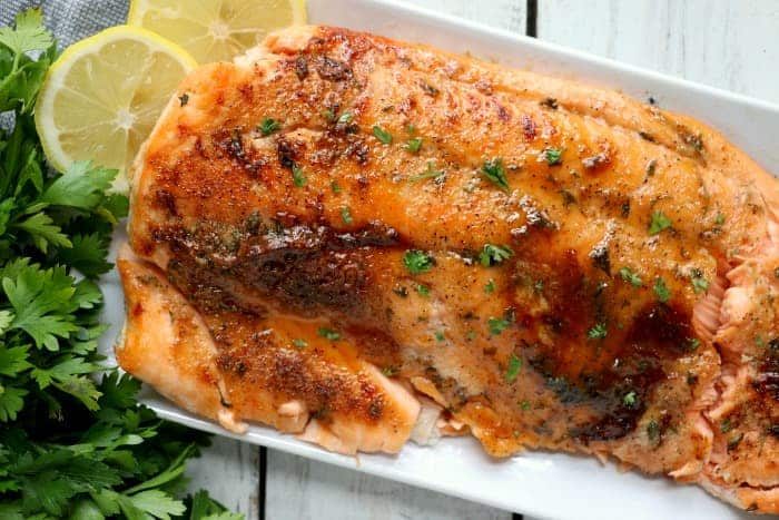 Dry rub salmon fillet with herbs and lemon slices on a white plate, perfectly crispy from the air fryer, garnished with fresh parsley.