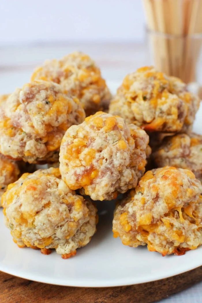 A plate of baked sausage balls with cheese, crafted from biscuit mix, piled together on a white dish.