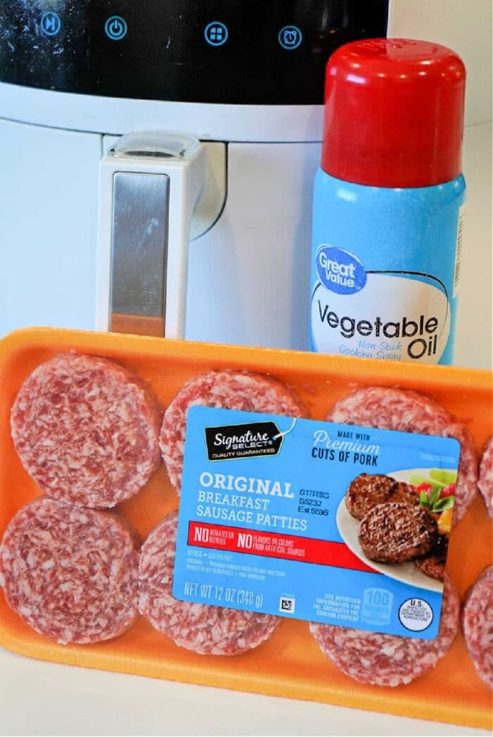 A tray of raw sausage patties and a can of vegetable oil sit next to an air fryer, ready for you to make good sausage patties in air fryer with ease.