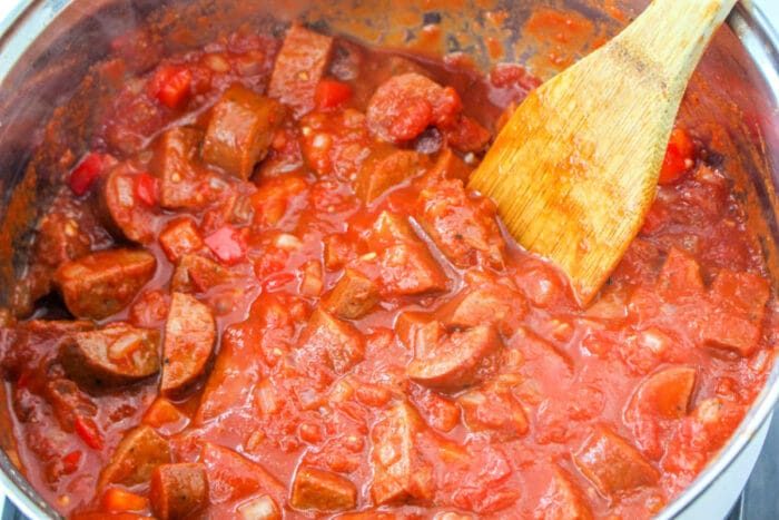 A pot of chunky tomato sauce with sausages sits invitingly, its rich aroma filling the air. Next to it, a wooden spoon rests, ready to twirl into a solid blend reminiscent of sausage spaghetti.