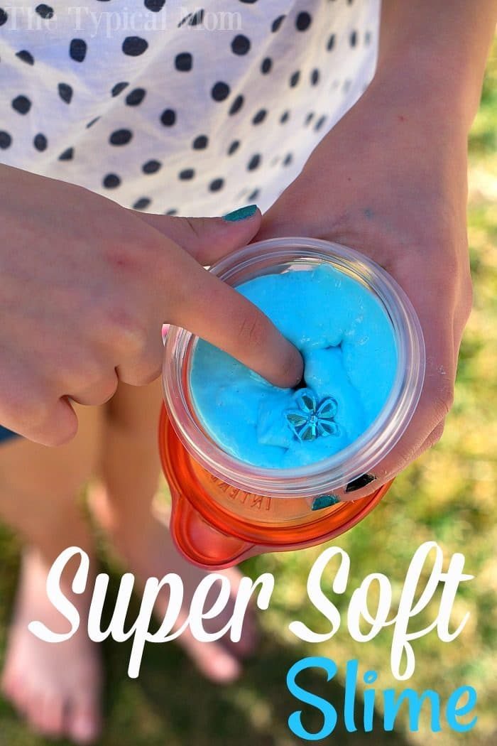 A person pokes blue slime in a clear container. The ground and feet are visible in the background. Text reads Super Soft Slime, made using our special soft slime recipe.