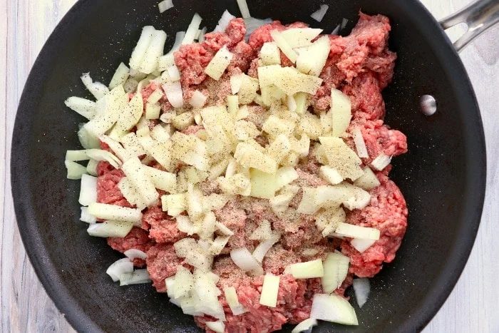 Chopped onions and ground meat sizzle in a black frying pan, seasoned with pepper