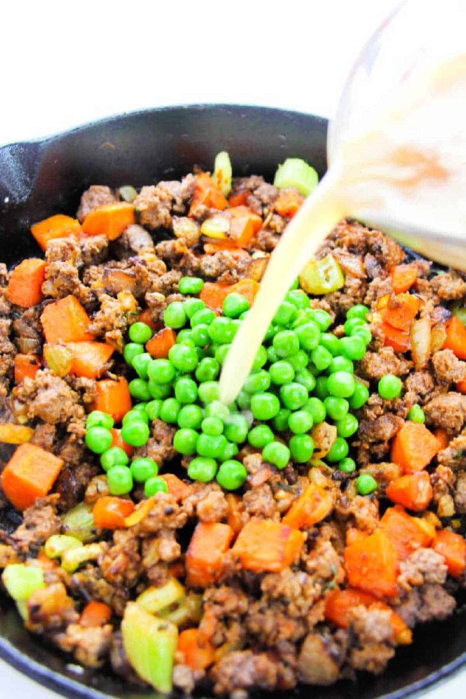 Ground beef, diced carrots, celery, and peas sizzle in a skillet as broth is poured over the mixture—the solid filling for a classic Shepherd's Pie with Instant Potatoes.
