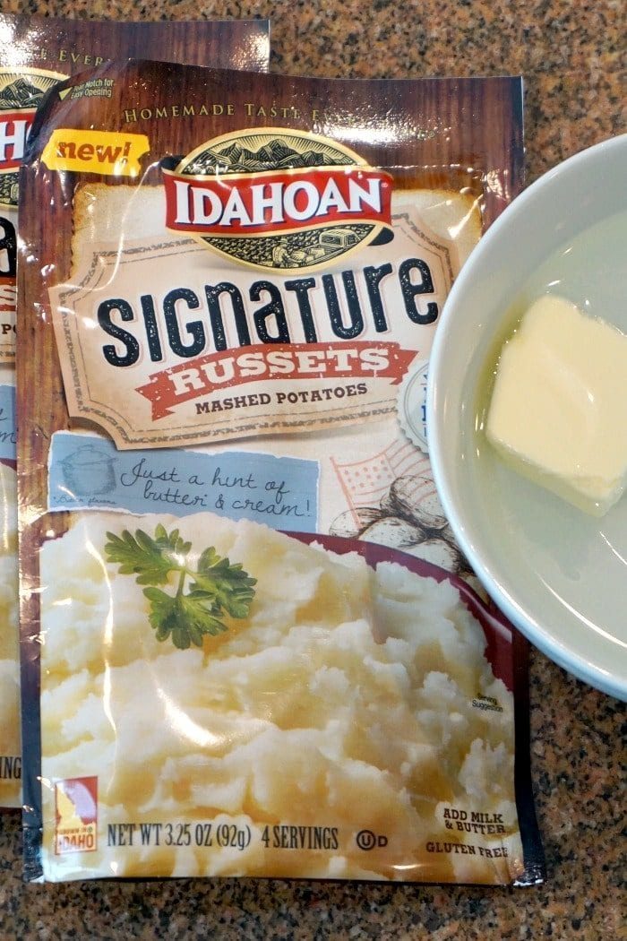 Packet of Idahoan Signature Russets mashed potatoes next to a small dish with a pat of butter on a countertop—solid for making Shepherd's Pie with Instant Potatoes.