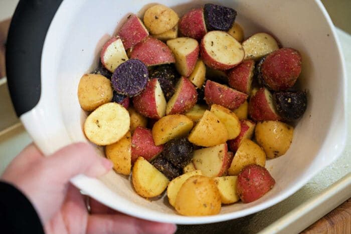 A bowl of seasoned, chopped red, yellow, and purple potatoes is ready for roasting—solid to pair with shrimp and potatoes for a hearty meal.
