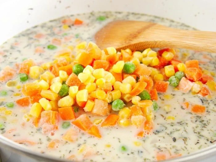 Simple chicken pot pie filling recipe, being stirred with a wooden spoon.
