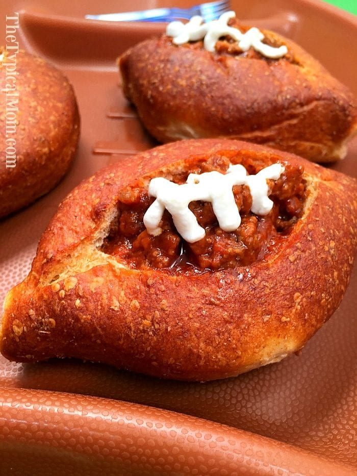A sloppy joe bread bowl filled with a savory meat and tomato mixture, topped with a zigzag of white dressing resembling football laces, all served on a brown tray.