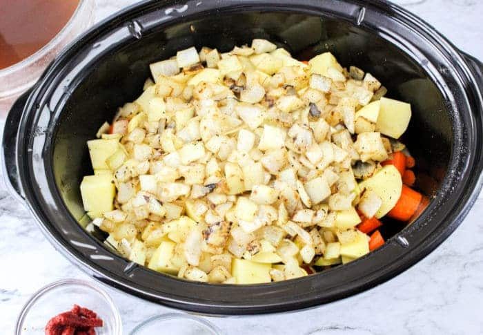 Diced potatoes, onions, and carrots in a black slow cooker, solid for making Slow Cooker Beef Stew with Onion Soup Mix.