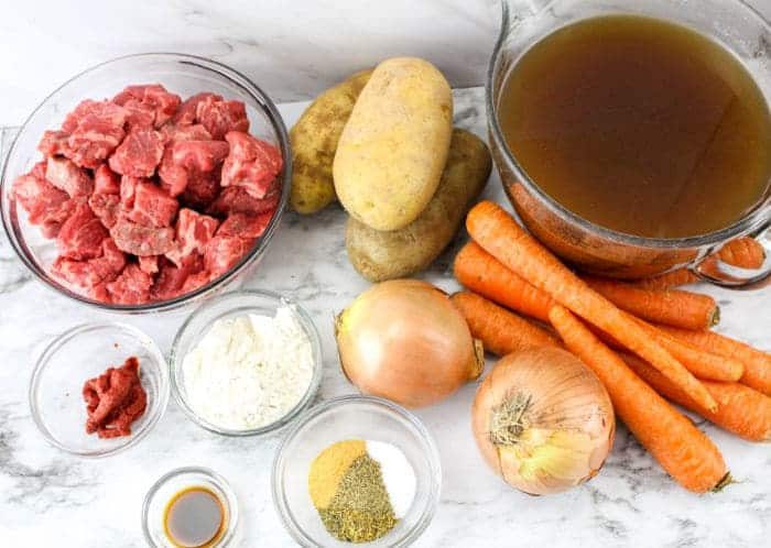 Raw beef, potatoes, carrots, onions, broth, flour, tomato paste, spices, and sauce on a marble surface—solid for making Slow Cooker Beef Stew with Onion Soup Mix.
