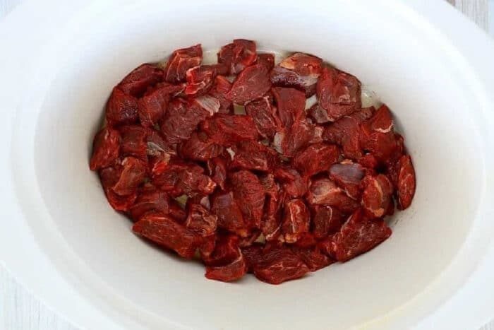 Raw beef chunks arranged in a white slow cooker, solid for making tender slow cooker beef tips.