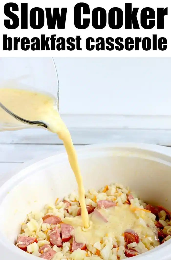 Egg mixture is poured into a slow cooker over chopped sausage, slow cooker cheesy potatoes, and cheese to make a hearty breakfast casserole.