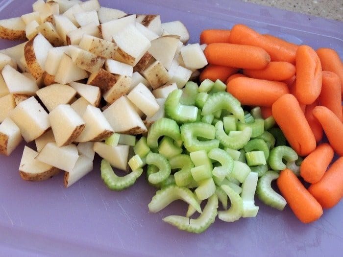 Chopped potatoes, celery slices, and baby carrots on a purple cutting board, solid for preparing slow cooker chicken and dumplings.