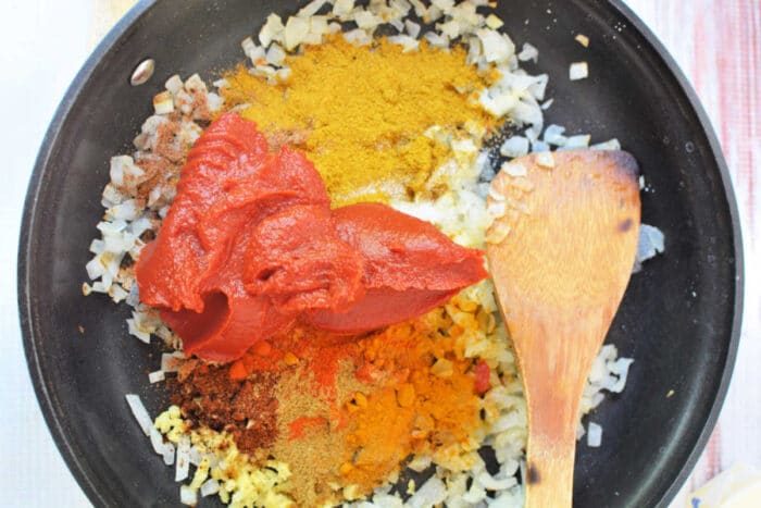 Chopped onions, spices, and tomato paste in a skillet with a wooden spatula—solid for starting a rich Chicken Makhani before transferring to the slow cooker.