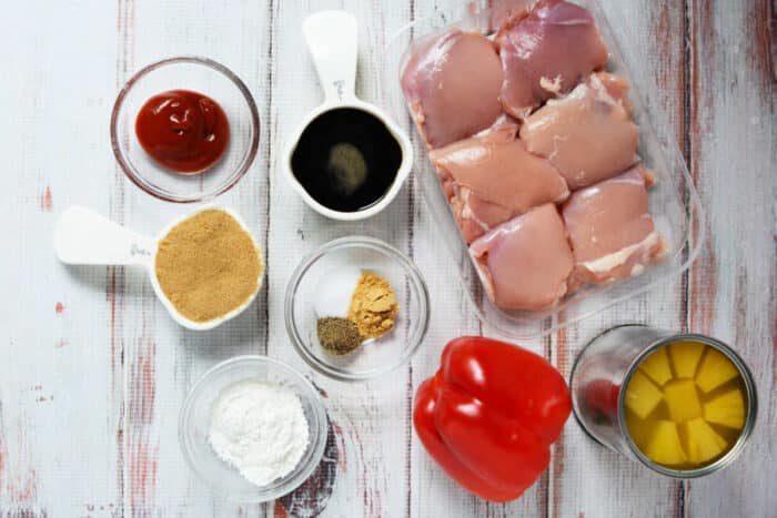Raw chicken thighs, red bell pepper, canned pineapple, and small bowls of ketchup, spices, soy sauce, cornstarch, and a splash of pineapple juice—solid for an easy Slow Cooker Chicken recipe.