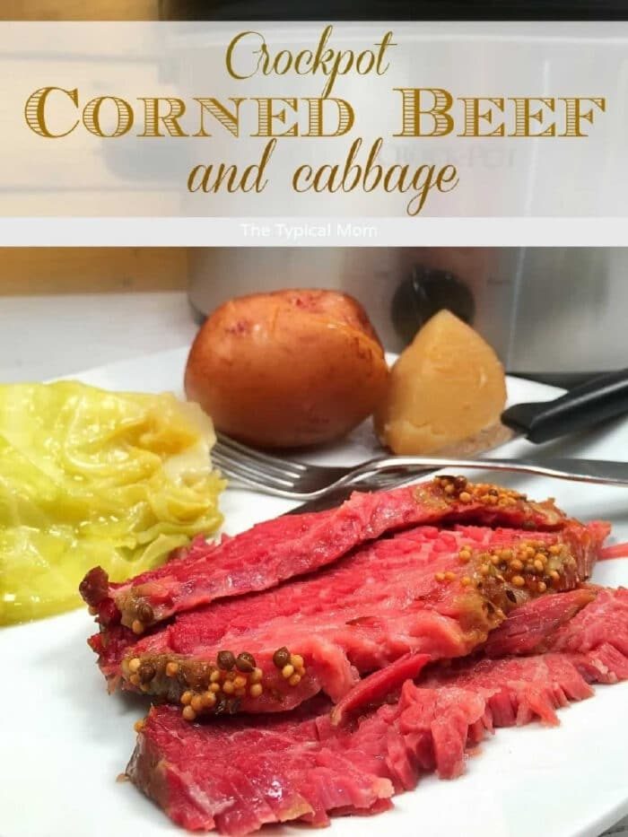 Sliced slow cooker corned beef brisket with mustard seeds, cabbage, and potatoes on a plate in front of a crockpot.