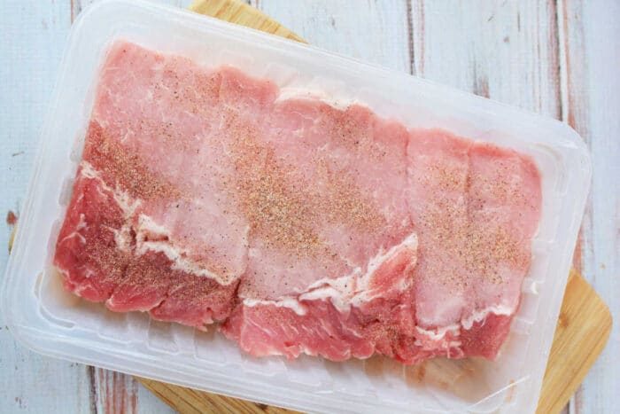 Raw boneless ribs in a plastic tray on a wooden surface, seasoned with spices like those used for slow cooker country style ribs.