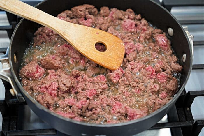 Ground beef being browned in a skillet on a stove, stirred with a wooden spatula—solid for starting a hearty slow cooker stroganoff.