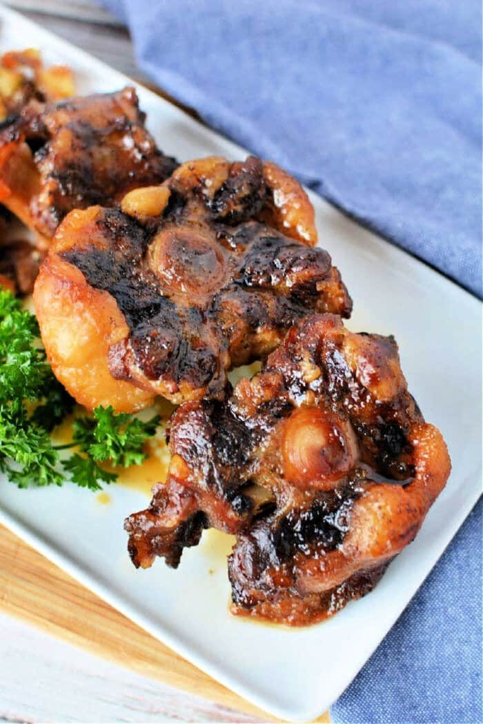 Close-up of oxtail pieces on a white plate, garnished with fresh parsley. This dish captures the rich flavors reminiscent of slow cooker oxtail perfection.