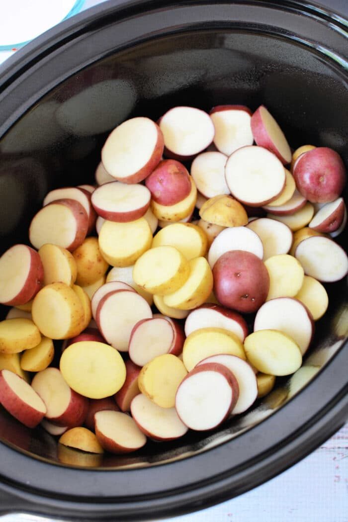 Sliced red and yellow potatoes in a black slow cooker, ready to be cooked—solid for Easy Potato Recipes or anyone searching for good Slow Cooker Potatoes.