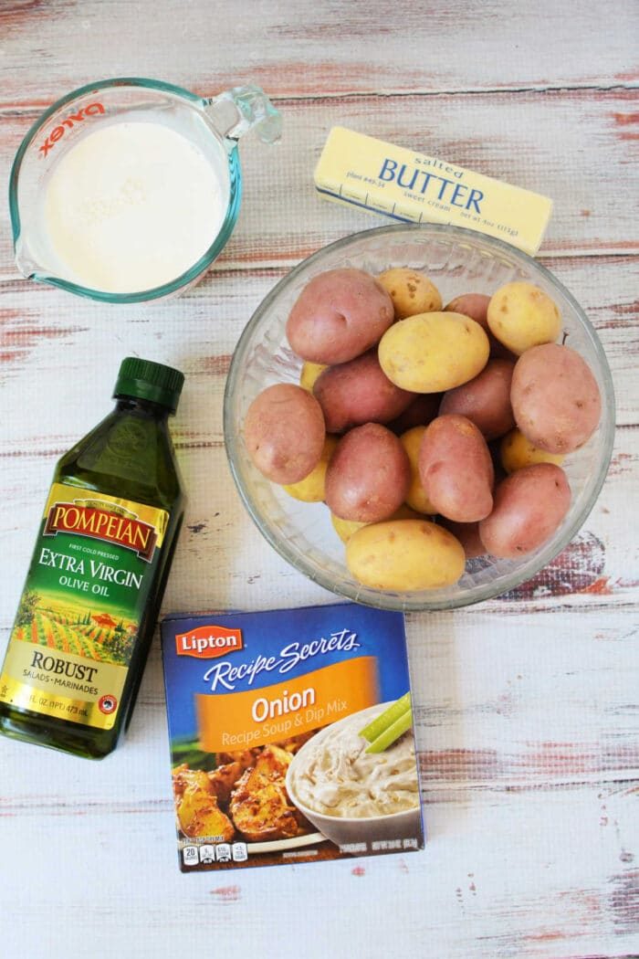 Bowl of potatoes, butter, milk, olive oil, and onion soup mix on a white wooden table—solid ingredients for trying good Slow Cooker Potatoes or adding to your favorite slow cooker recipes.