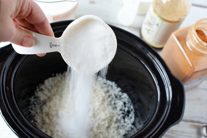 Pouring sugar into a slow cooker to create a creamy rice pudding.