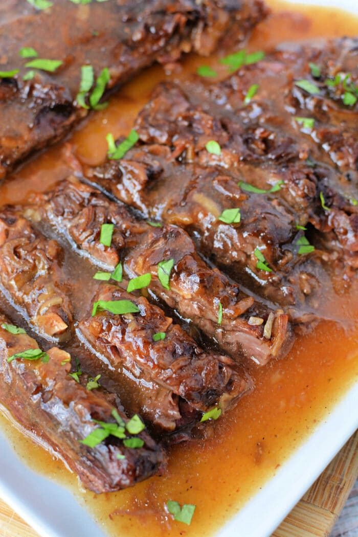 Sliced Slow Cooker Skirt Steak in rich brown gravy, garnished with chopped fresh parsley on a white serving platter.