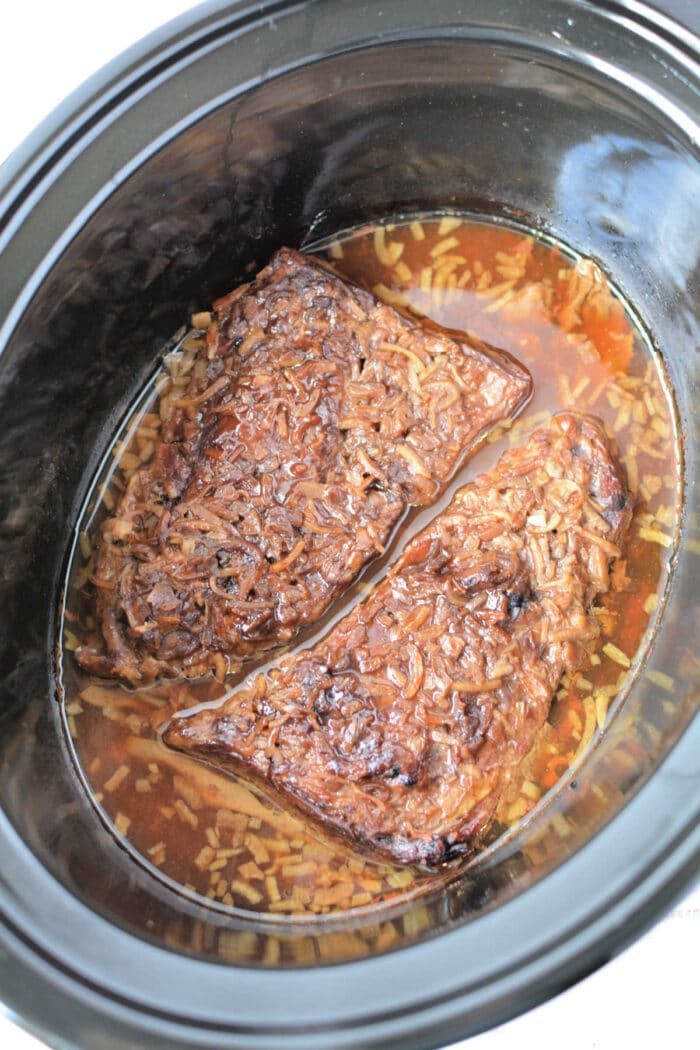Two pieces of beef brisket cook in a slow cooker with broth and seasonings, like you would prepare Slow Cooker Skirt Steak for tender, flavorful results.
