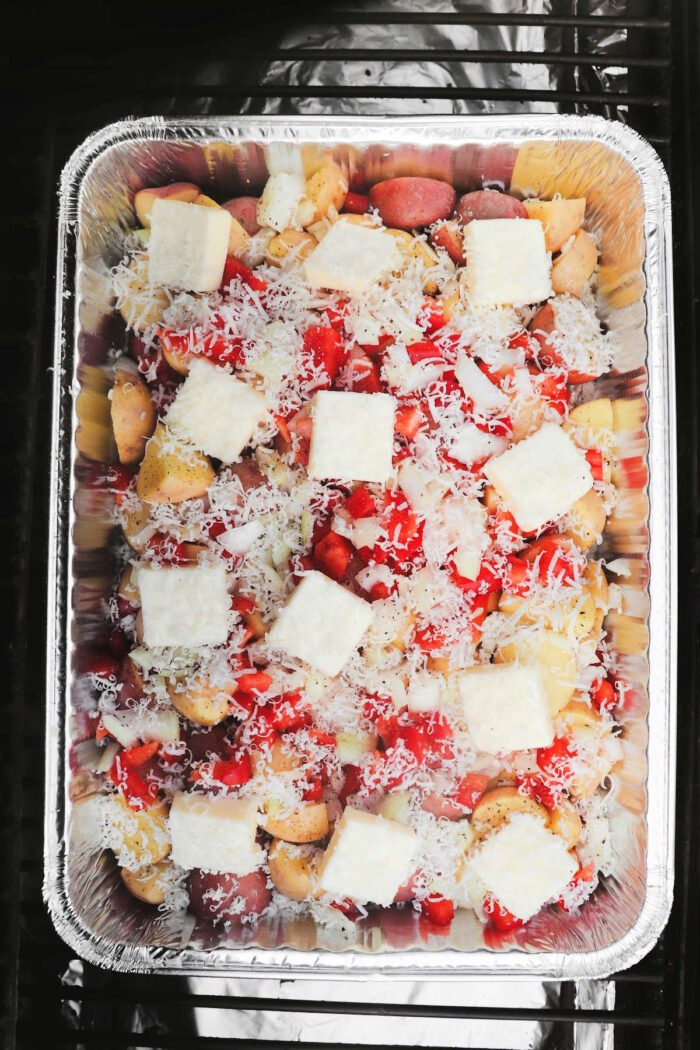 Foil pan filled with chopped vegetables, grated cheese, and cubed butter, solid for making smoked cheesy potatoes and ready to be cooked.