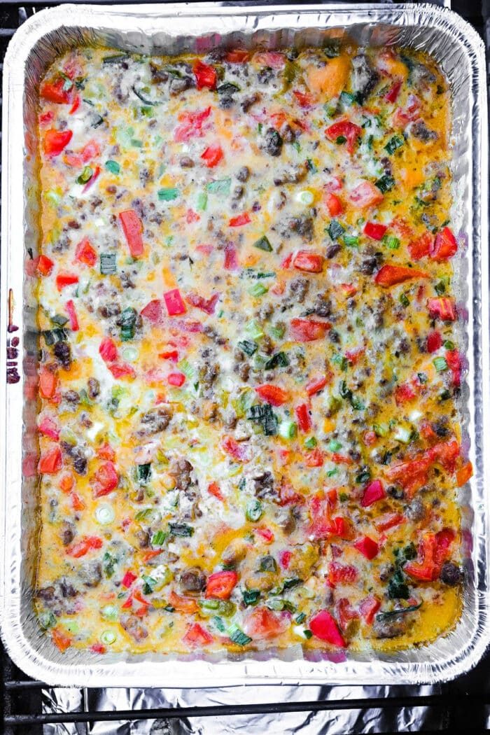 Smoked queso dip in a foil tray, topped with melted cheese, red peppers, green onions, and ground meat, reminiscent of a hearty Smoked Queso Dip.