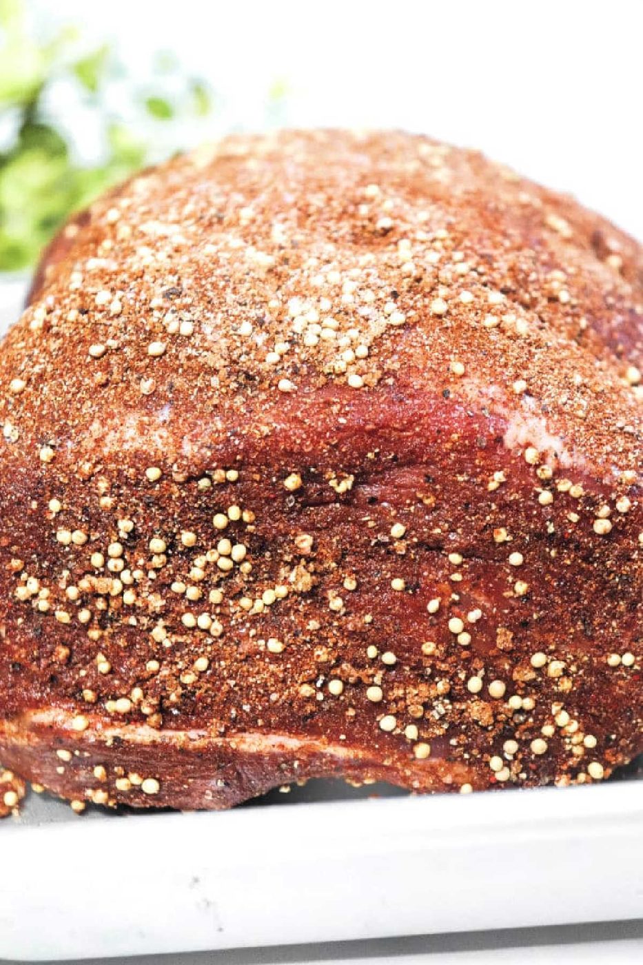 Smoked Sirloin Tip Roast coated in a spice rub and mustard seeds, resting on a white tray.